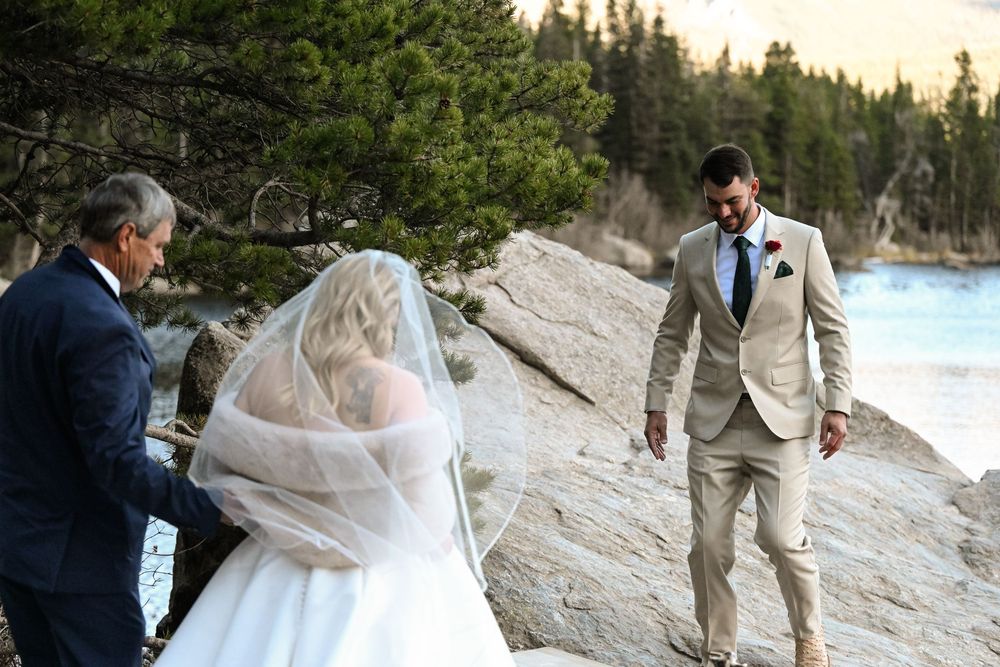A couple shares romantic moments during their beach wedding ceremony with pine trees and ocean views in the background.