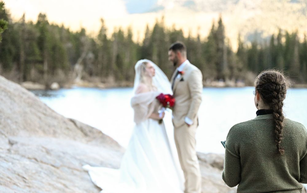 A romantic outdoor winter wedding ceremony with couple embracing against snowy mountain backdrop at sunset.