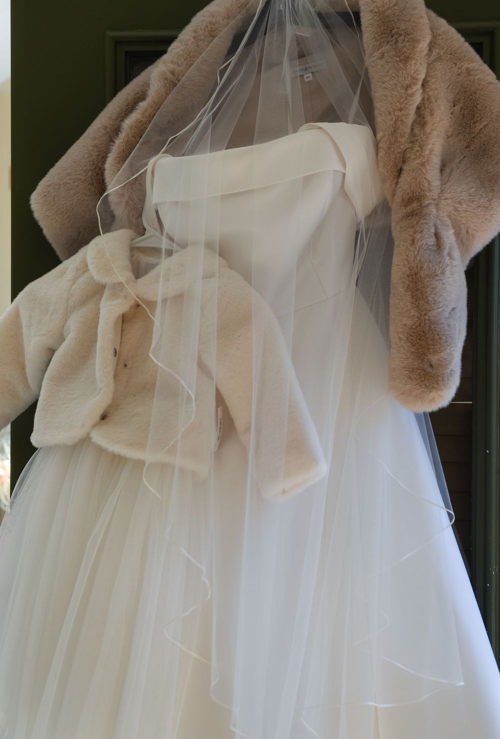 A close-up view of a white wedding dress with delicate tulle layers and a beige fur stole draped across the top.