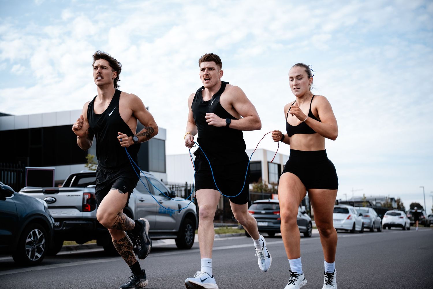 Athletes in black workout attire run together in formation on an outdoor track during training.