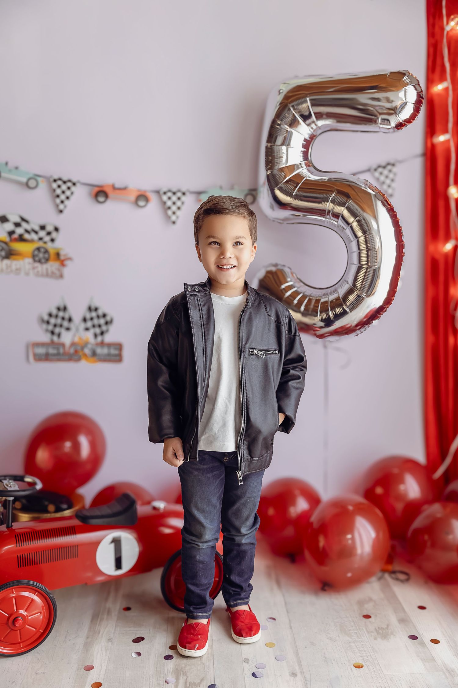 El numero 5 en forma de globo en la parte de atras con globos rojos y un carrito rojo de carrera nino de 5 anos sonriendo