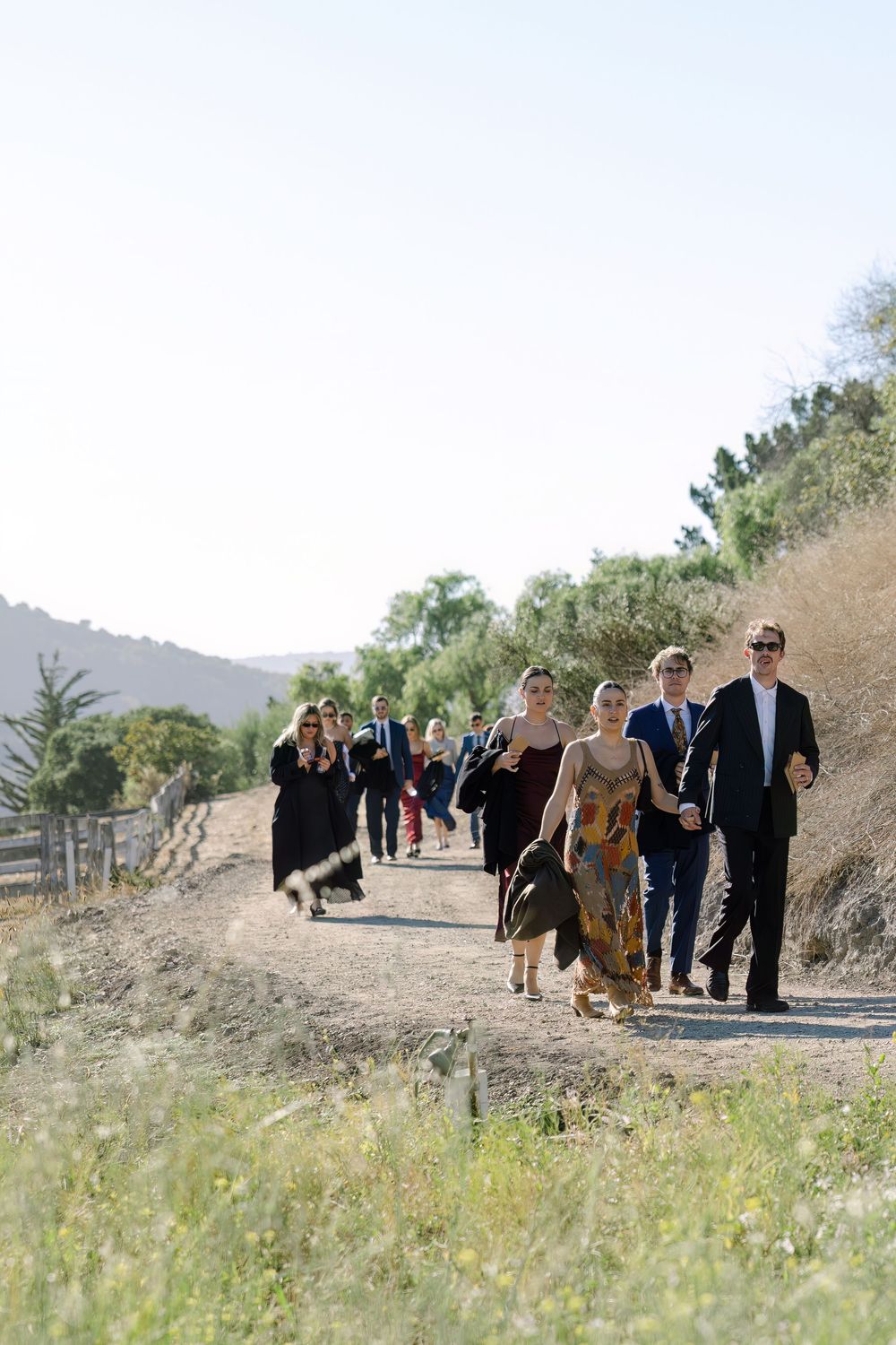 Wedding party walks along a winding path on a sunny hillside captured on film by Danielle Conner Photography in Carmel Valley, Ca.