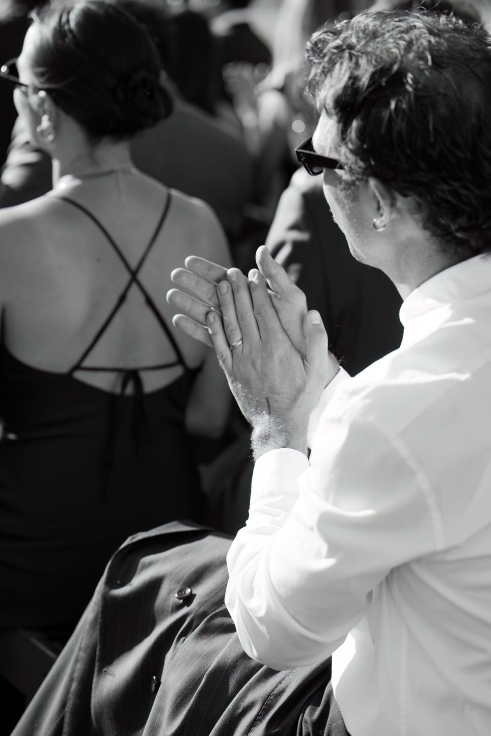 Emotional guests in formal attire react during a touching moment at an outdoor wedding ceremony.