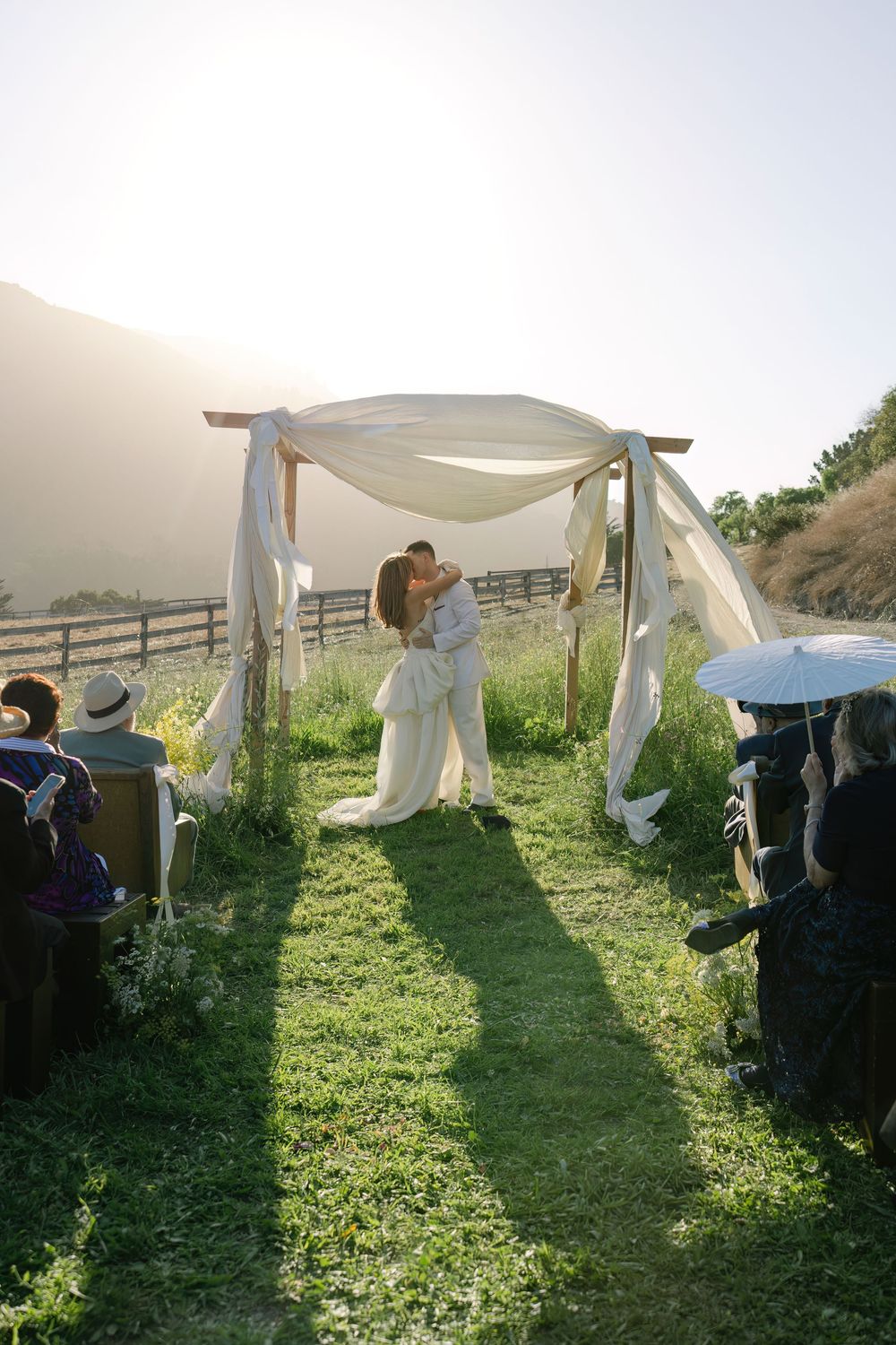 People work together to arrange white fabric draping on an outdoor wedding arch structure.
