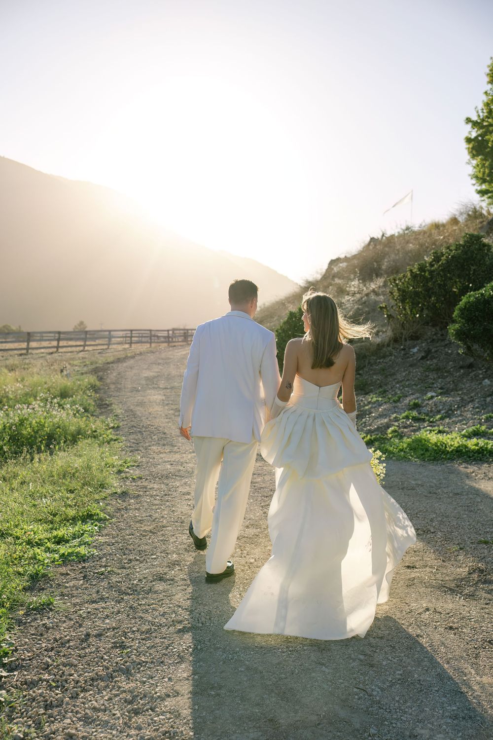 Couple walking hand in hand on a dirt path during sunset.