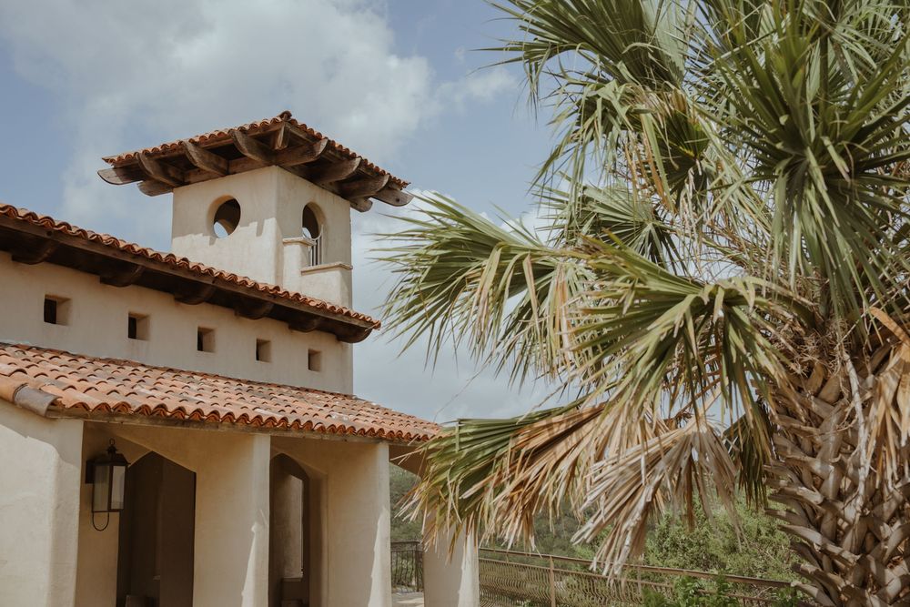 Spanish colonial style architecture with white walls and terra cotta roof tiles under palm trees.