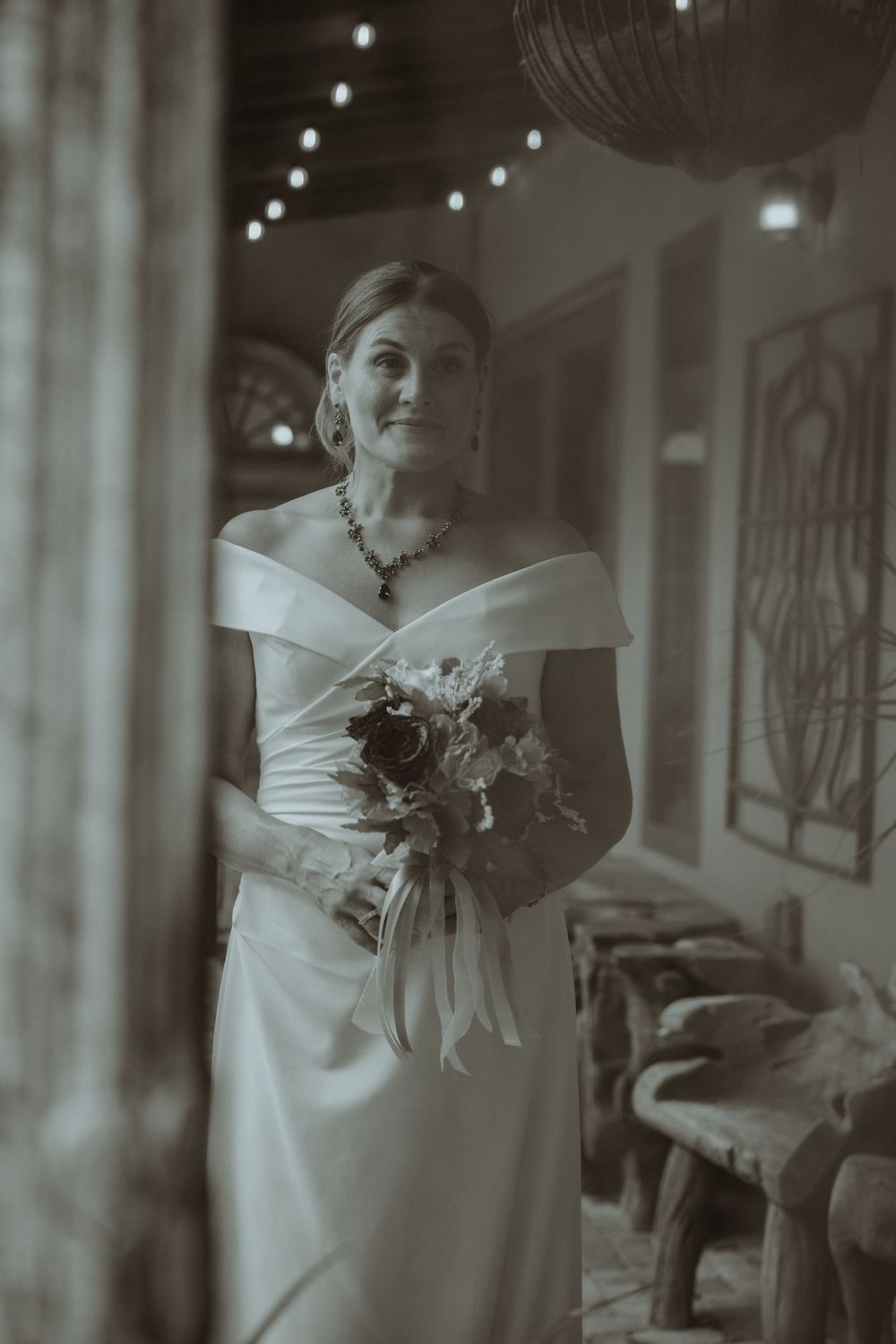 Artistic black and white portrait of bride holding bouquet in elegant indoor setting.