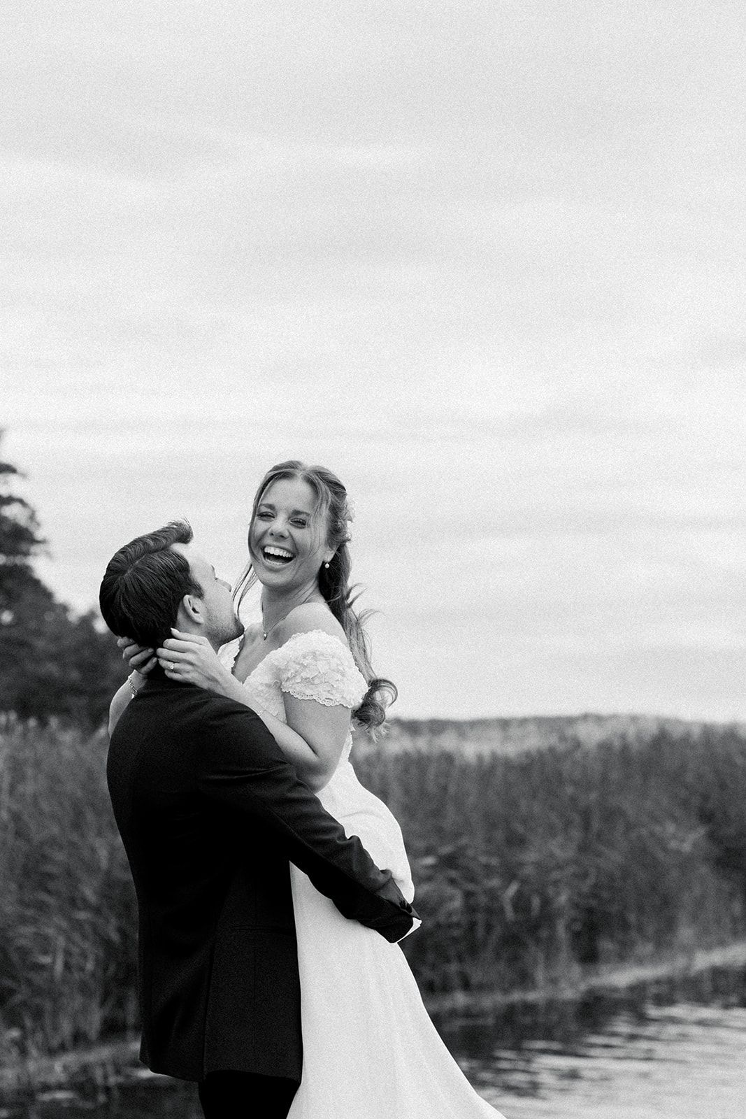 A joyful black and white wedding moment captured outdoors by a lake with the couple embracing in celebration.
