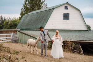 A rustic barn wedding venue with green metal roof set against a cloudy sky and evergreen trees.