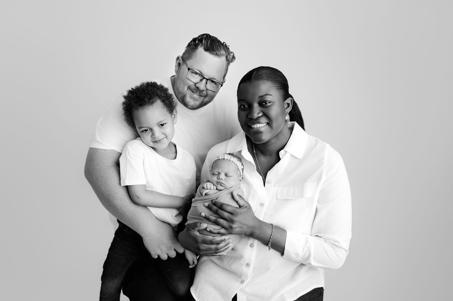 A black and white studio portrait of a loving family with their two young children.