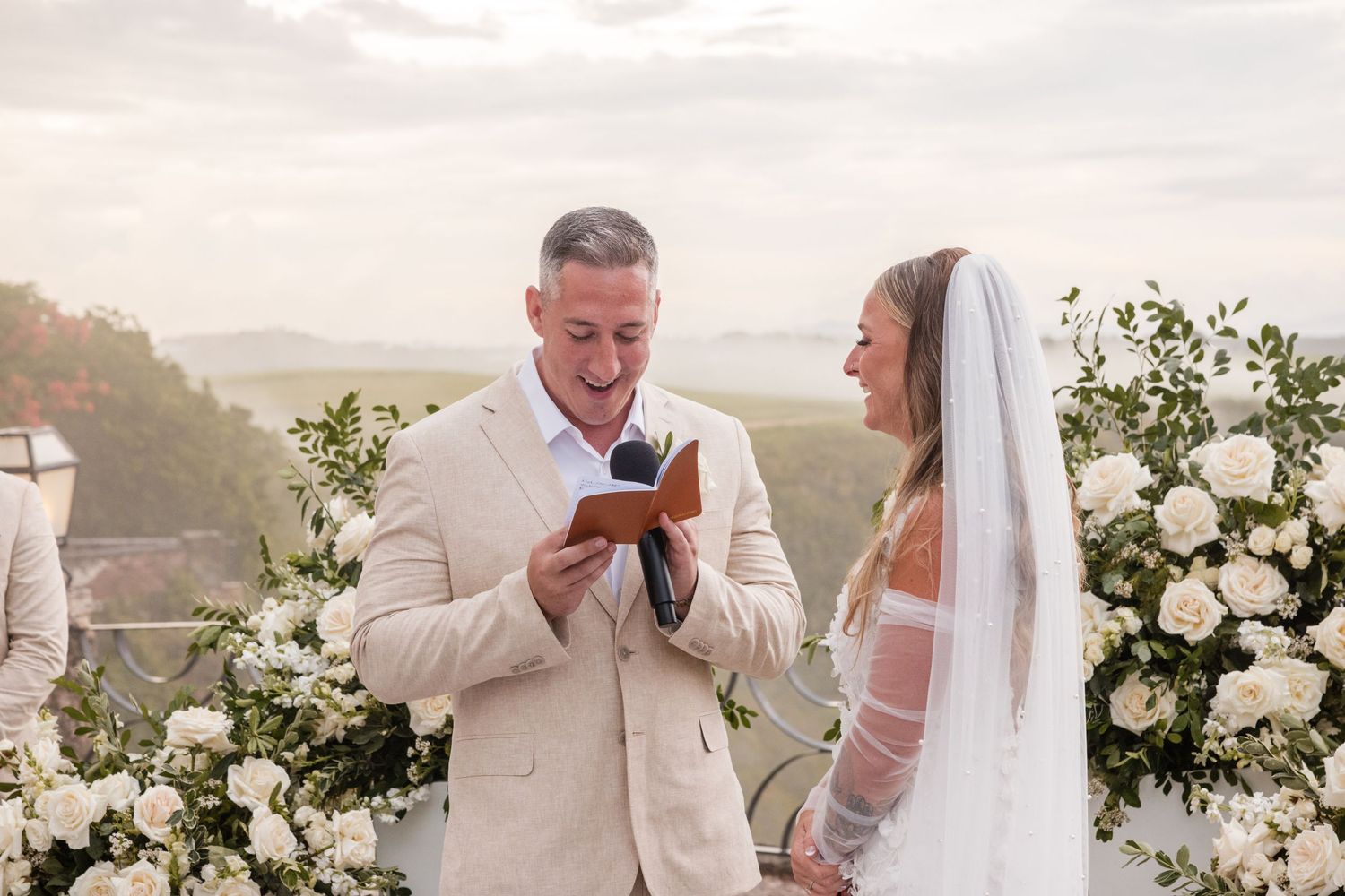 A wedding couple shares a sweet moment together on a beach with white floral arrangements and an ocean view.