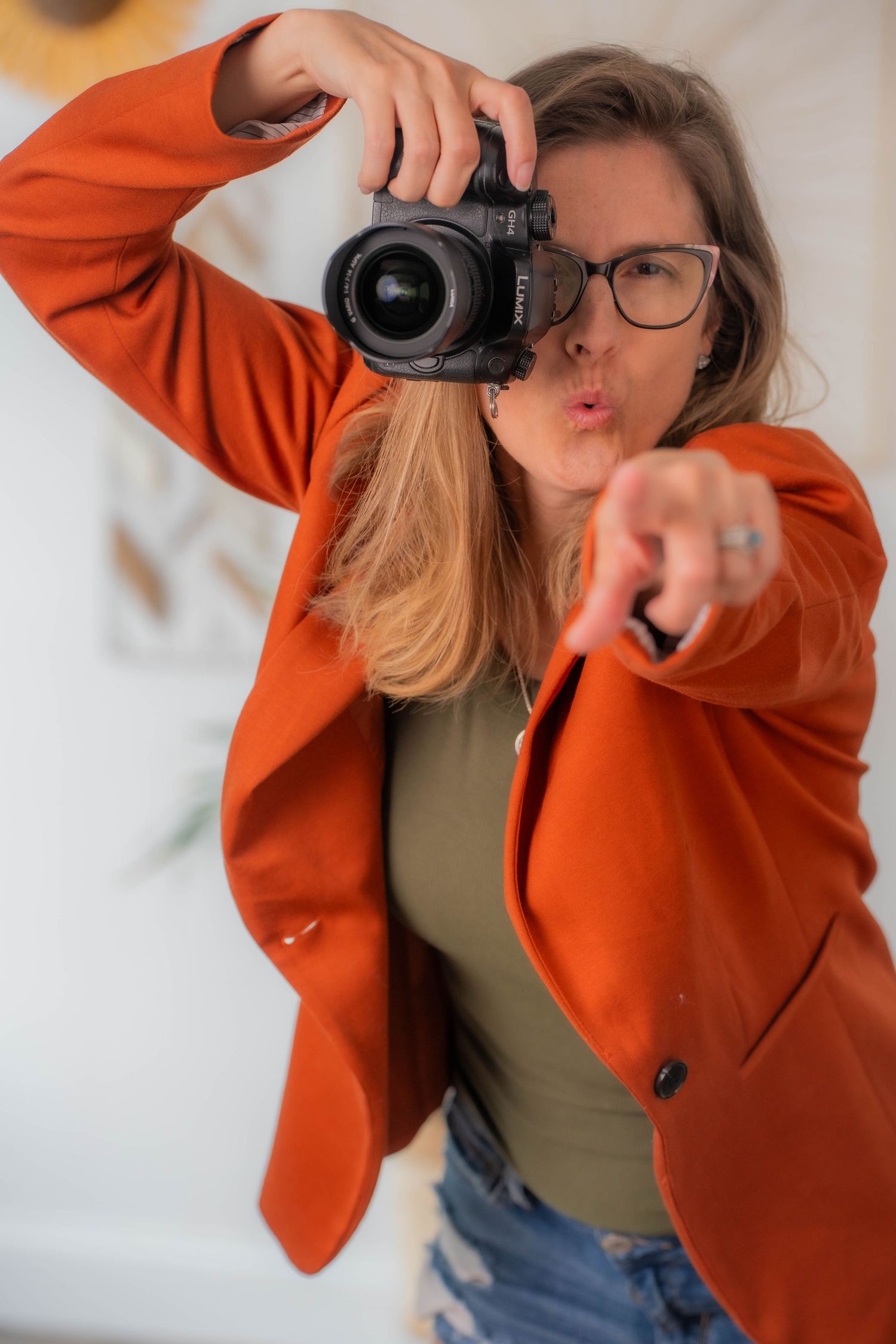 Nh Photographer in bright orange blazer taking creative selfie with professional camera.