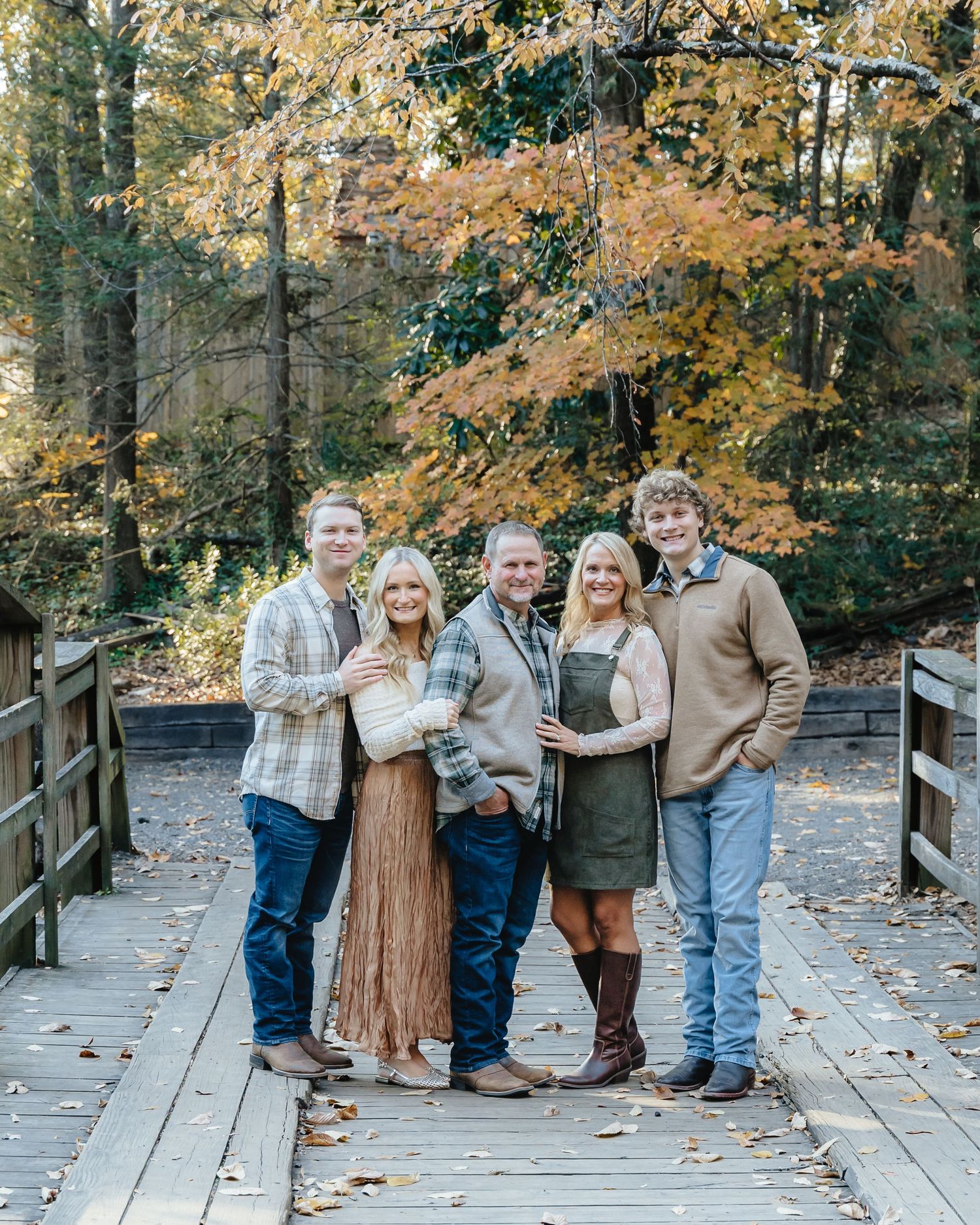 Family poses on wooden bridge during fall family photoshoot with autumn foliage.