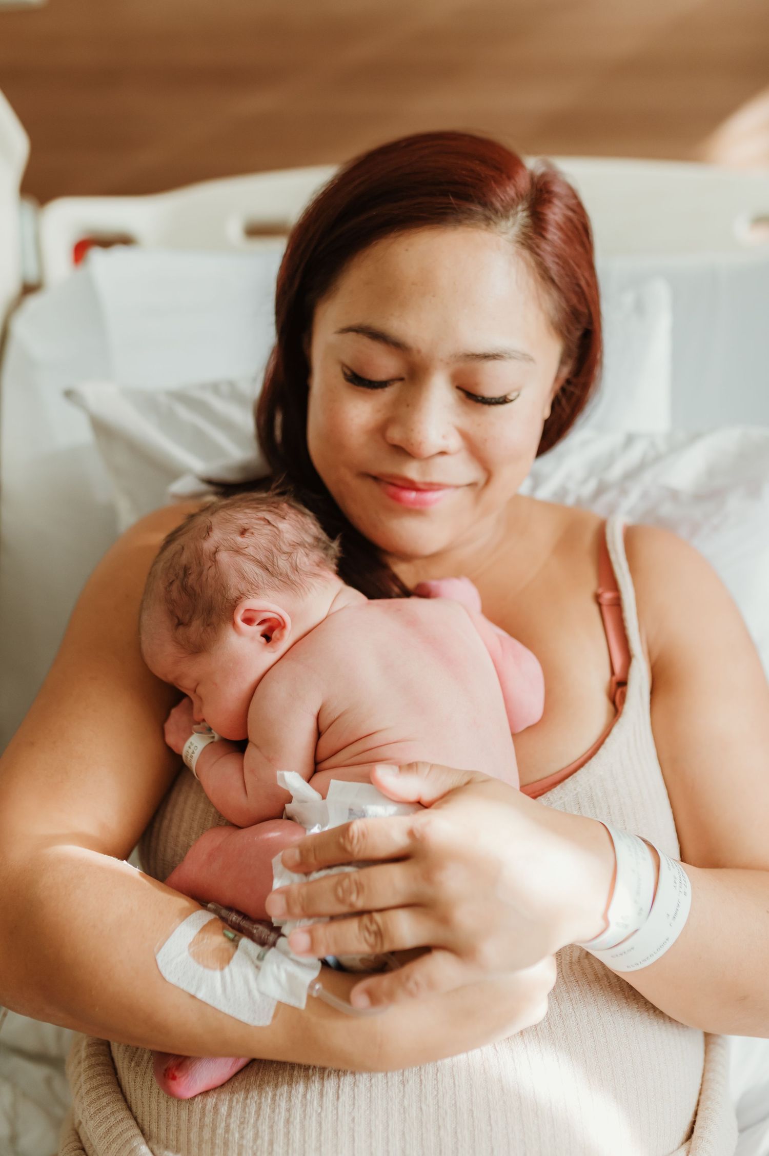 A tender moment captured as a mother holds her newborn baby close while resting on white bedding.