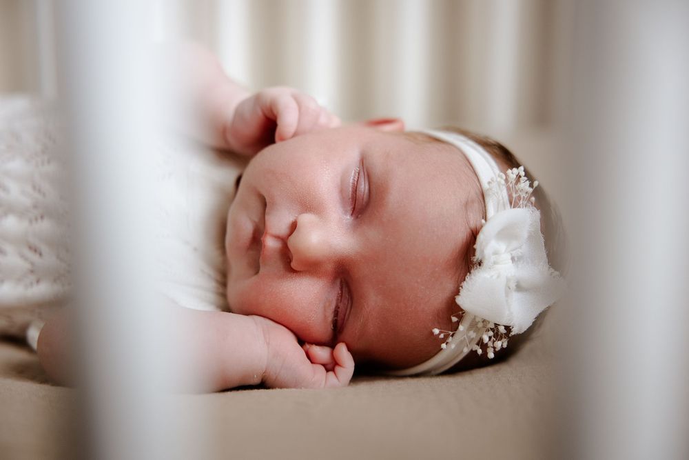 Gentle portrait of sleeping infant through white crib slats.
