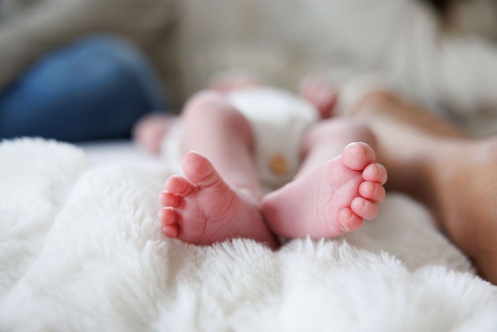 Newborn baby feet resting on soft white furry blanket.