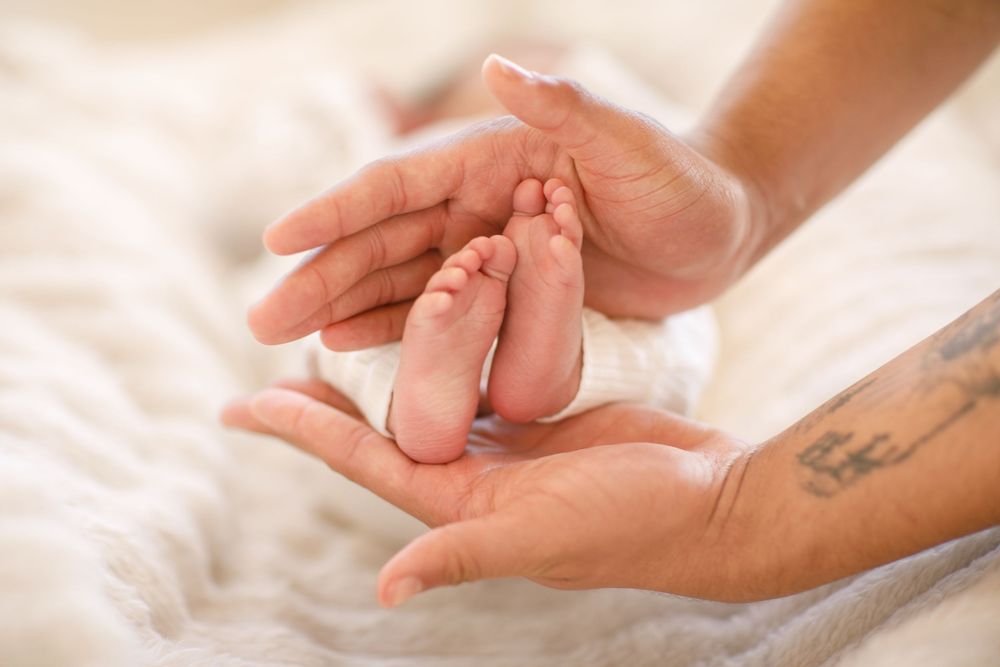 Close-up of gentle hands holding newborn baby on soft white fabric.