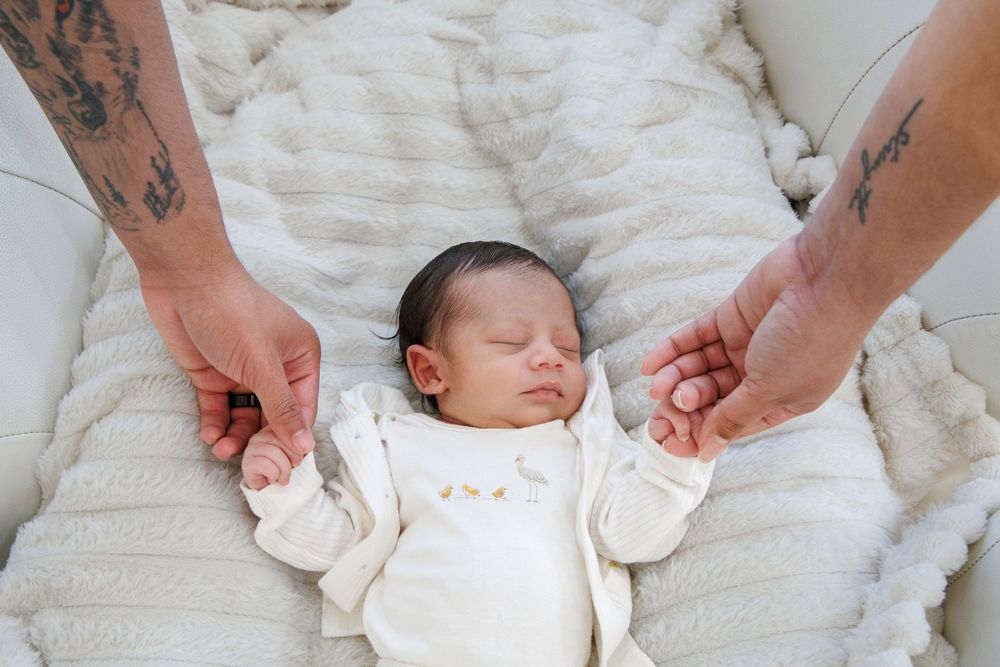 A newborn baby swaddled in white fabric being gently held against a textured white background.