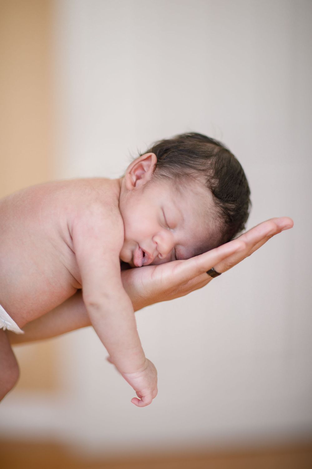 A sleeping newborn baby resting peacefully on outstretched hands against a light background.
