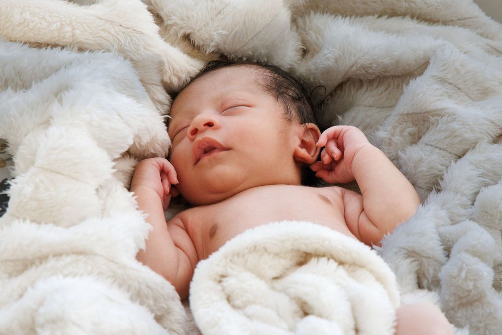 A sleeping infant nestled in soft white blankets during a professional photoshoot.