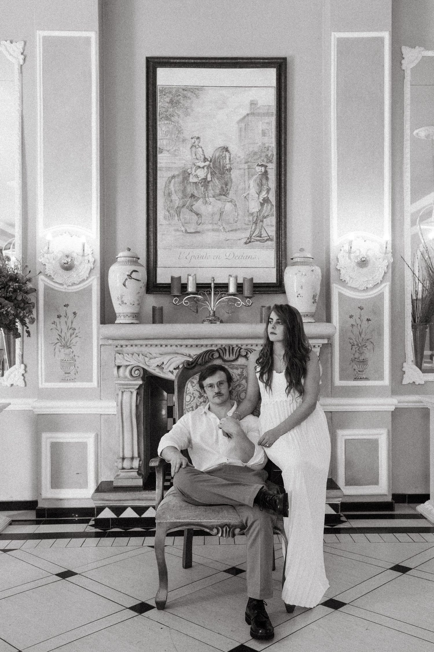A couple dances playfully in an elegant room with ornate wall panels and framed artwork.