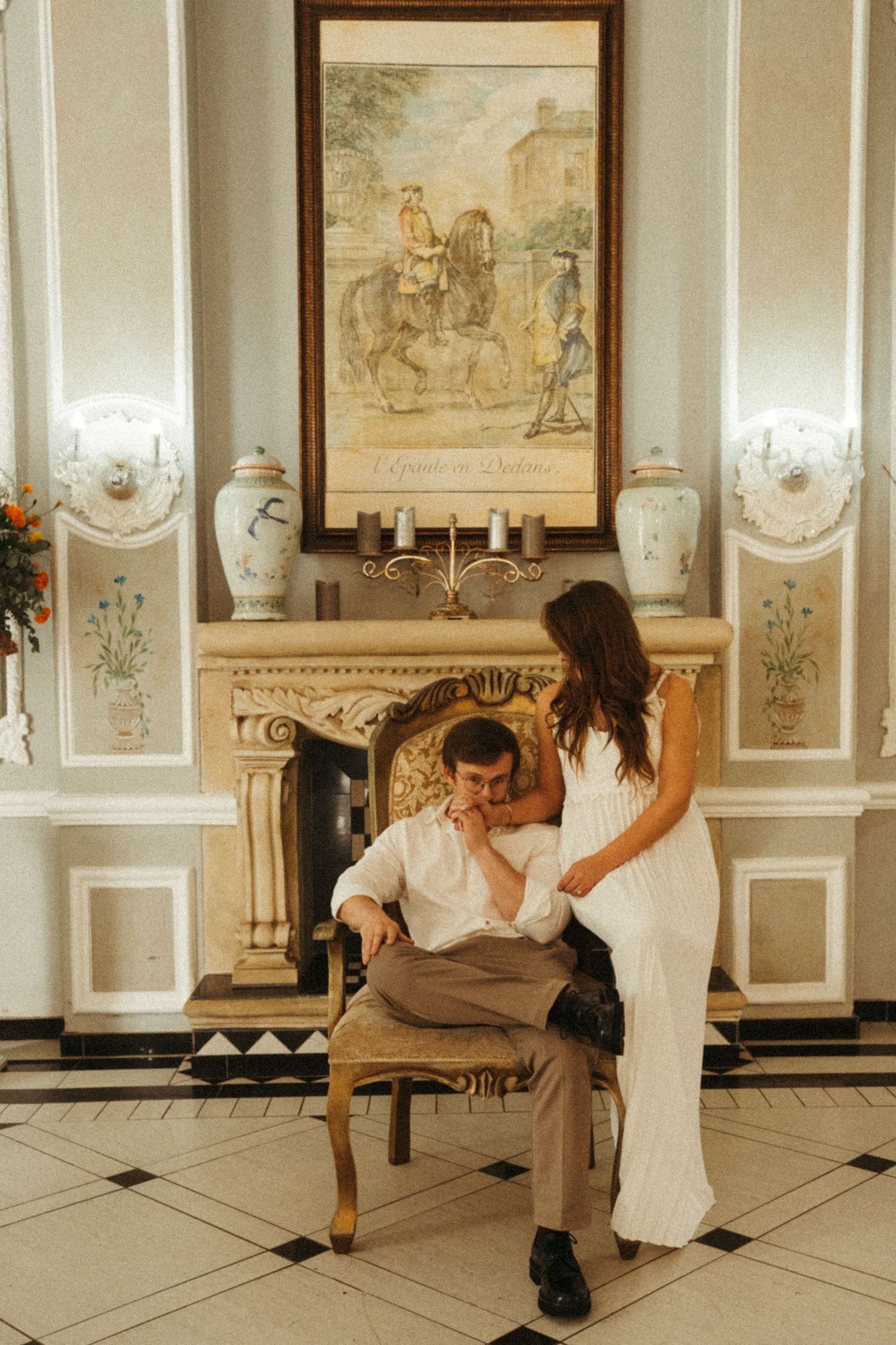 A couple performs dance moves in a classical interior with white paneled walls.