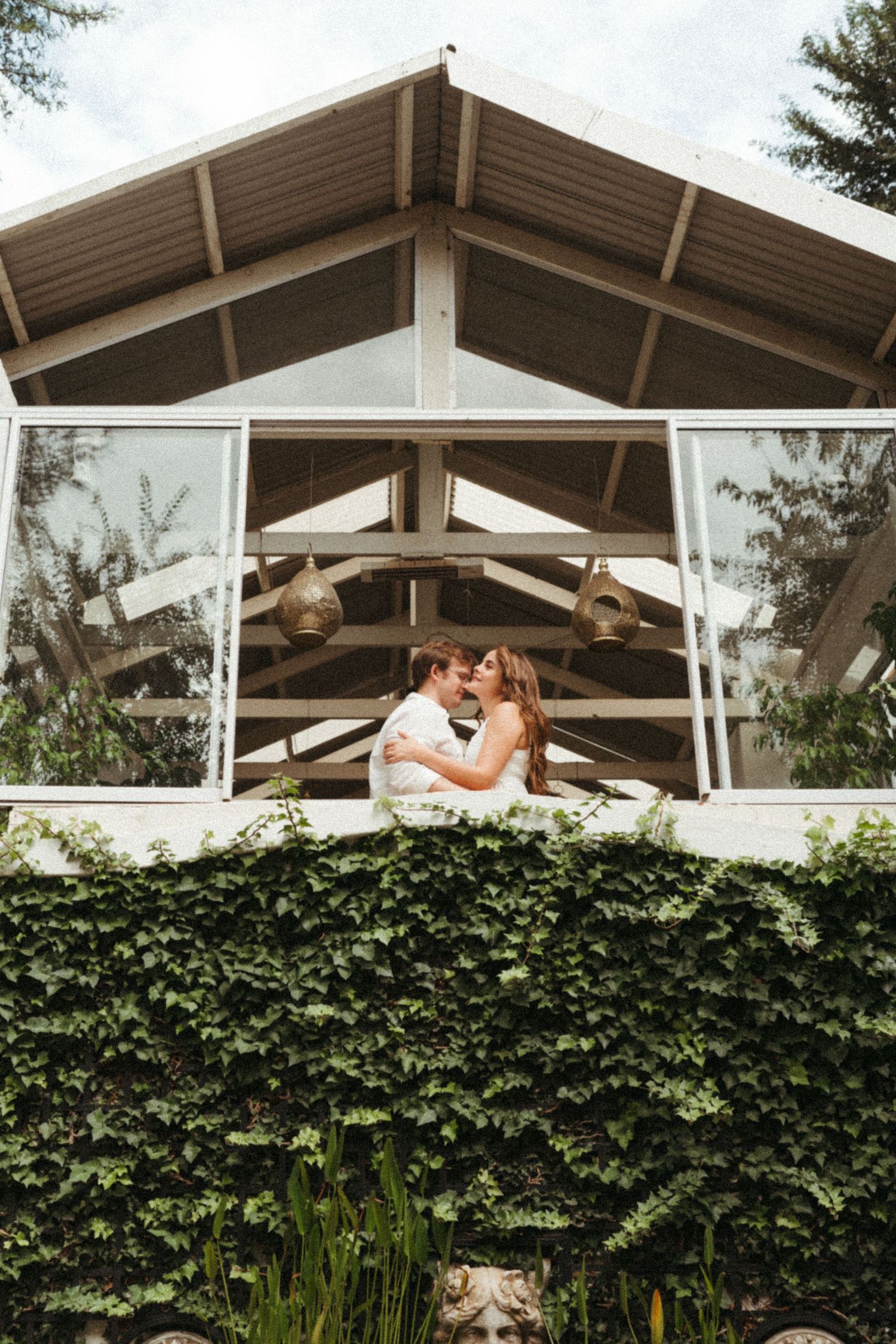 A couple shares an intimate moment on a balcony with ivy-covered walls below.
