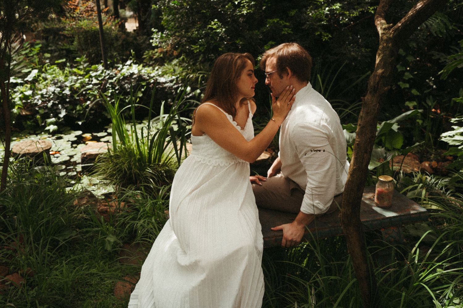 A couple shares romantic moments in a lush garden setting with natural lighting.