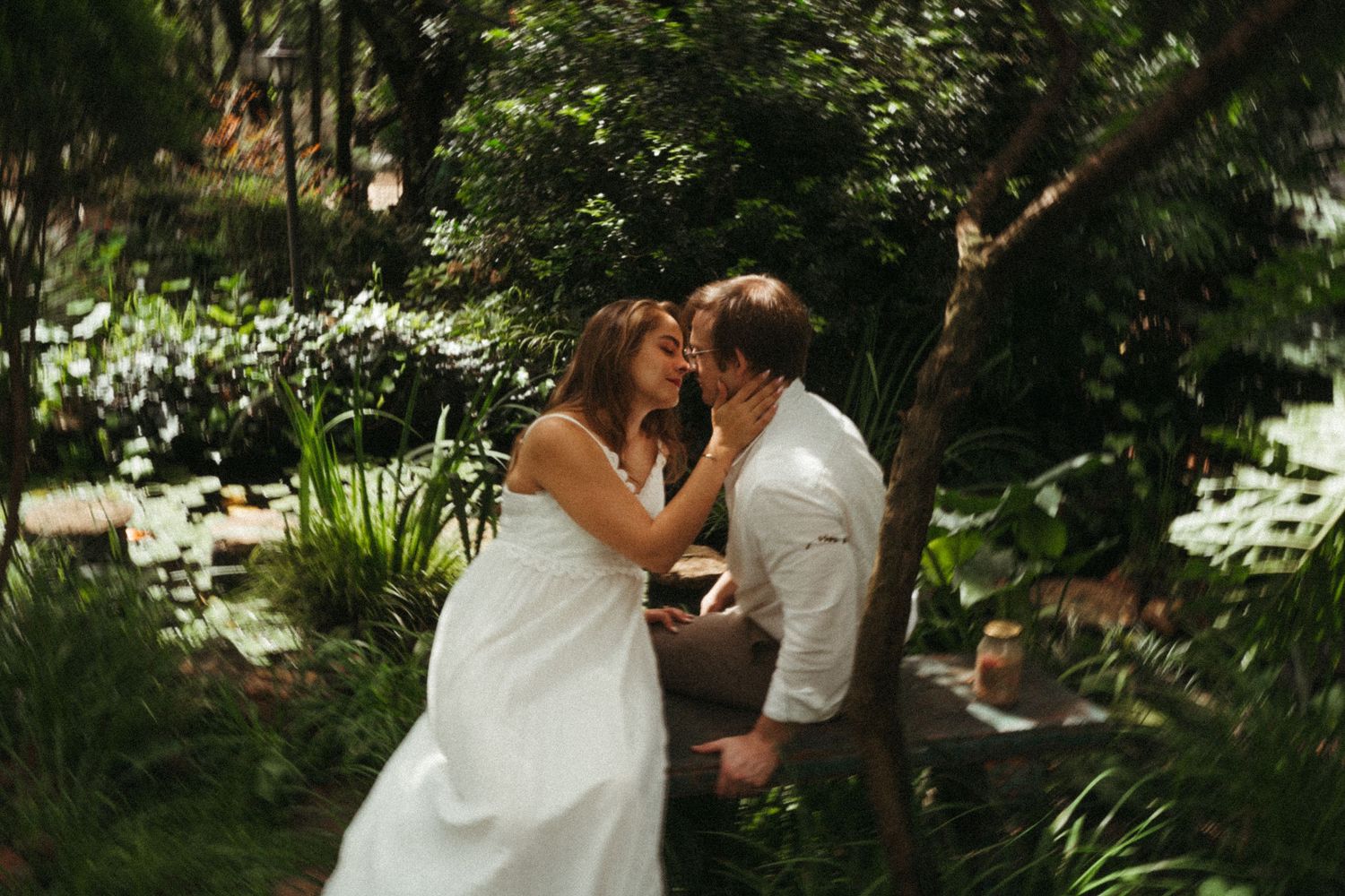 A couple embraces in a serene garden setting surrounded by lush greenery.