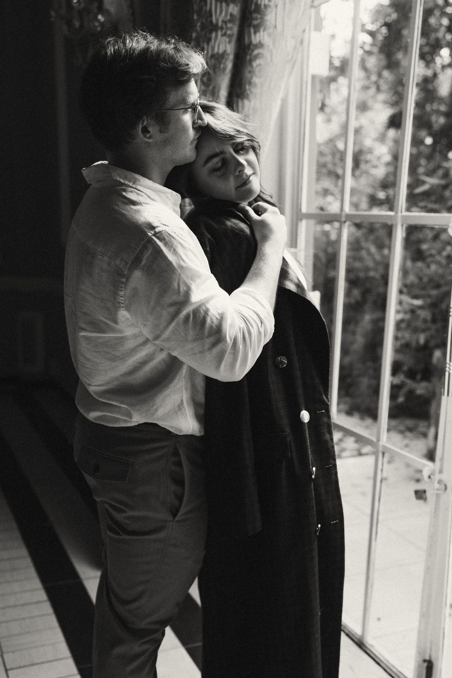 A series of black and white photographs showing a couple's tender interaction by a window.