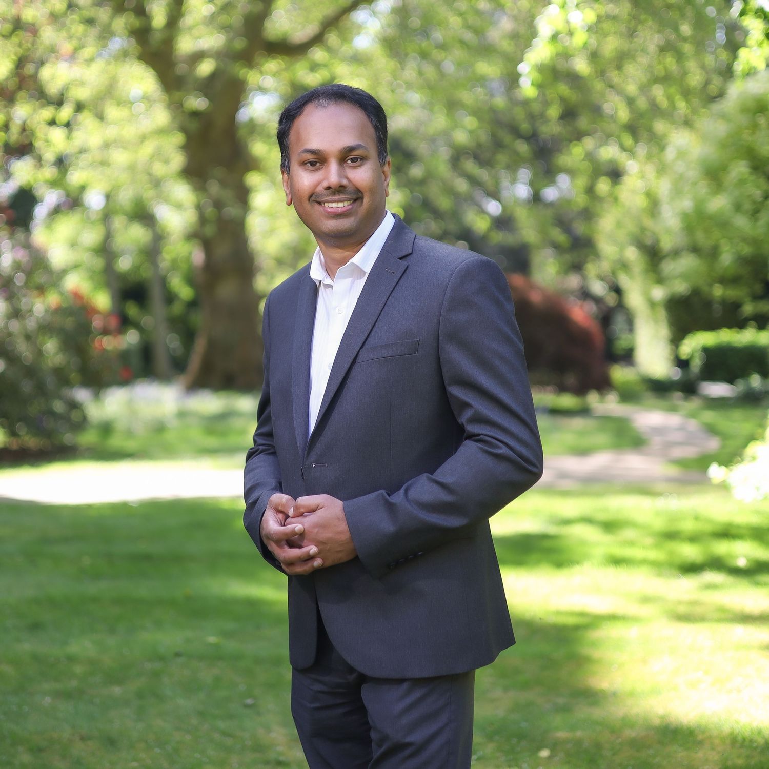 Business professional portrait in navy suit with white shirt against garden background.