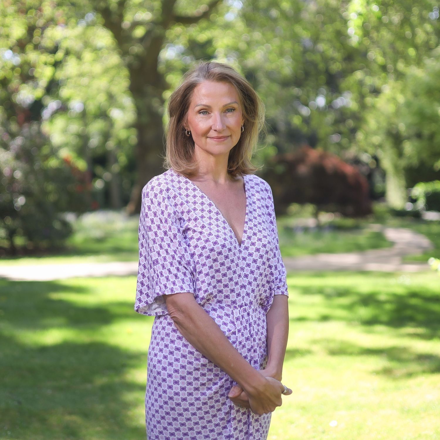 A person in a polka dot dress poses in a sunny outdoor garden setting.