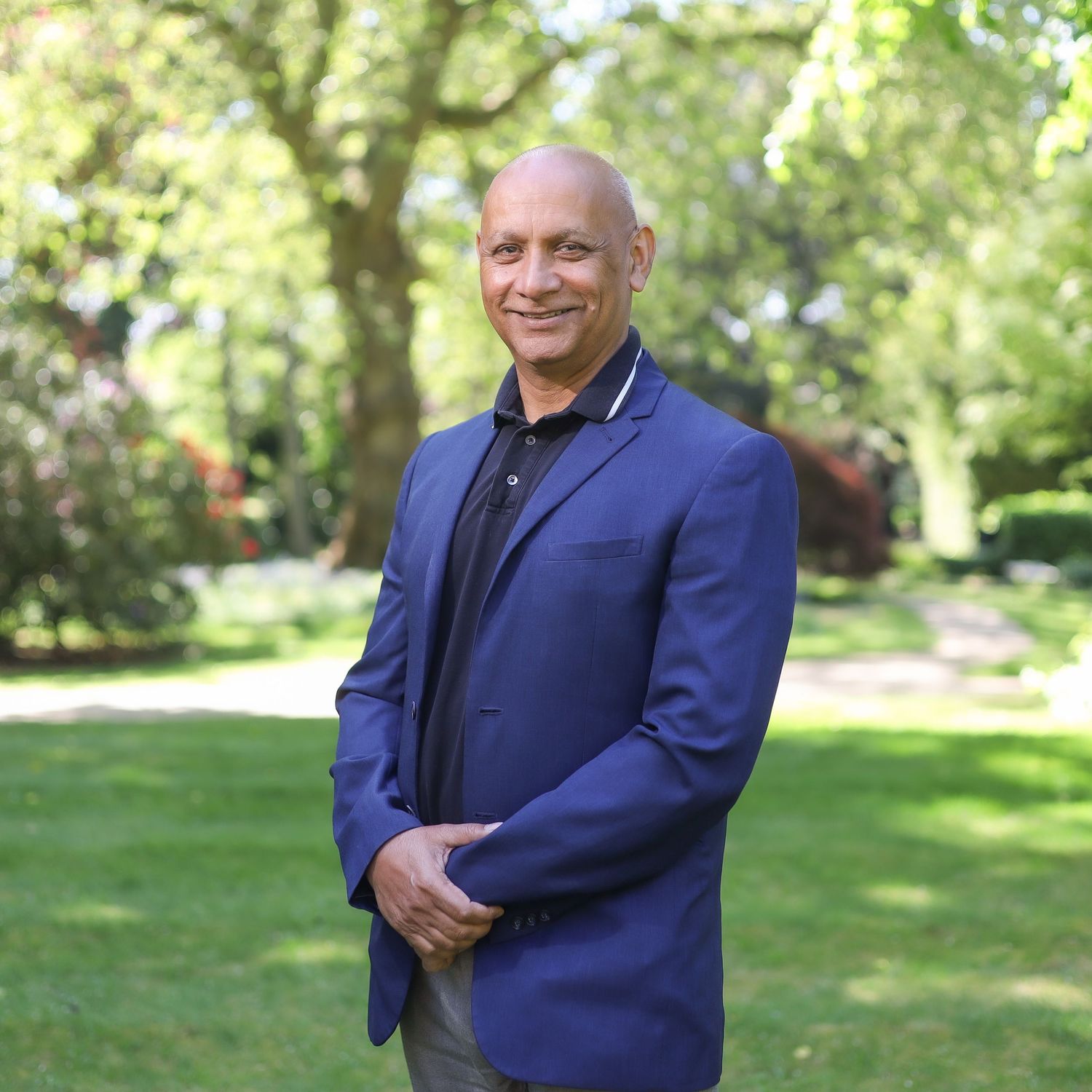Professional headshots of person in navy suit against blurred green garden background.