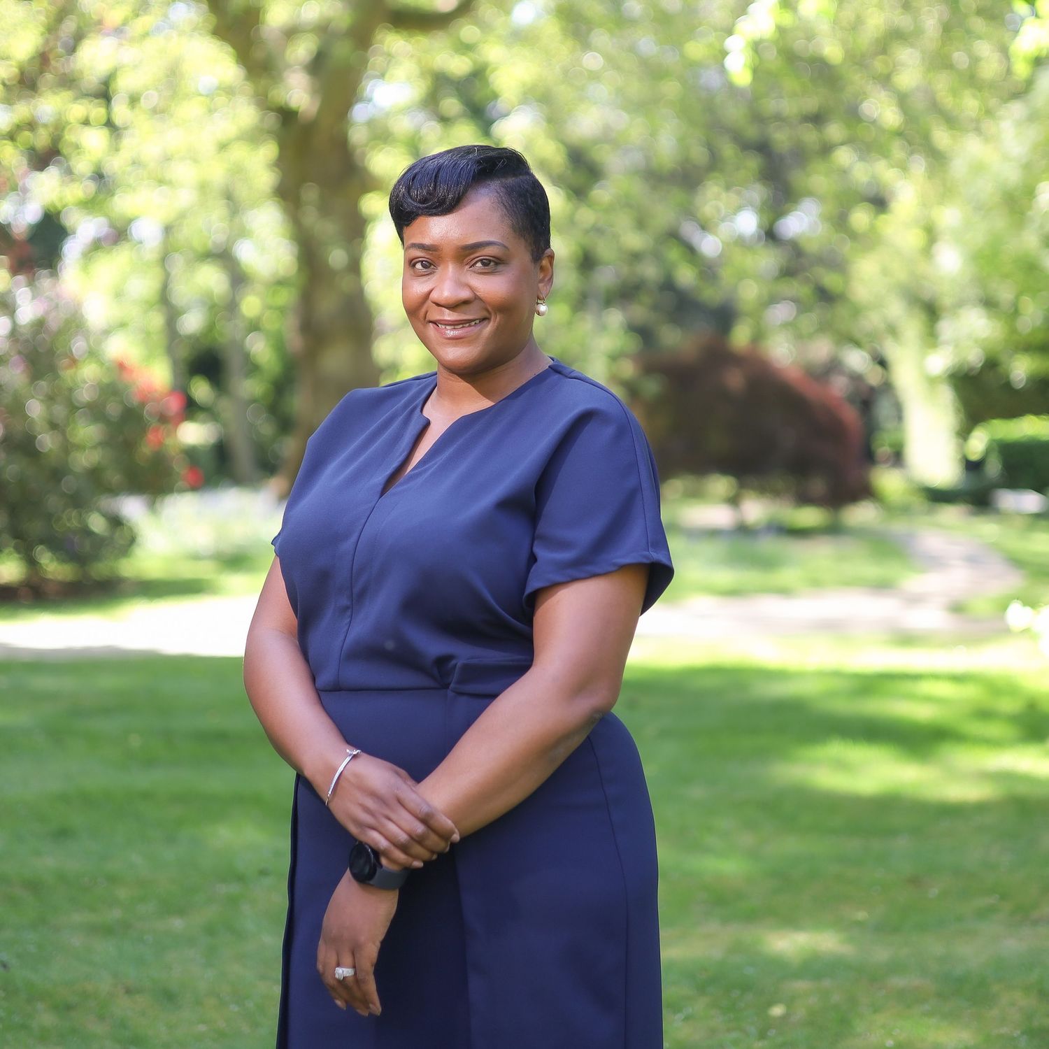 Professional portrait in navy blue dress standing in a sunny garden setting.