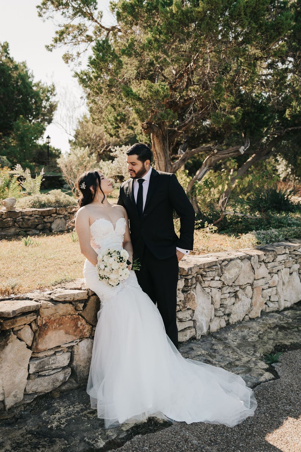 Wedding couple shares intimate moment by stone wall during outdoor photo session in natural setting.