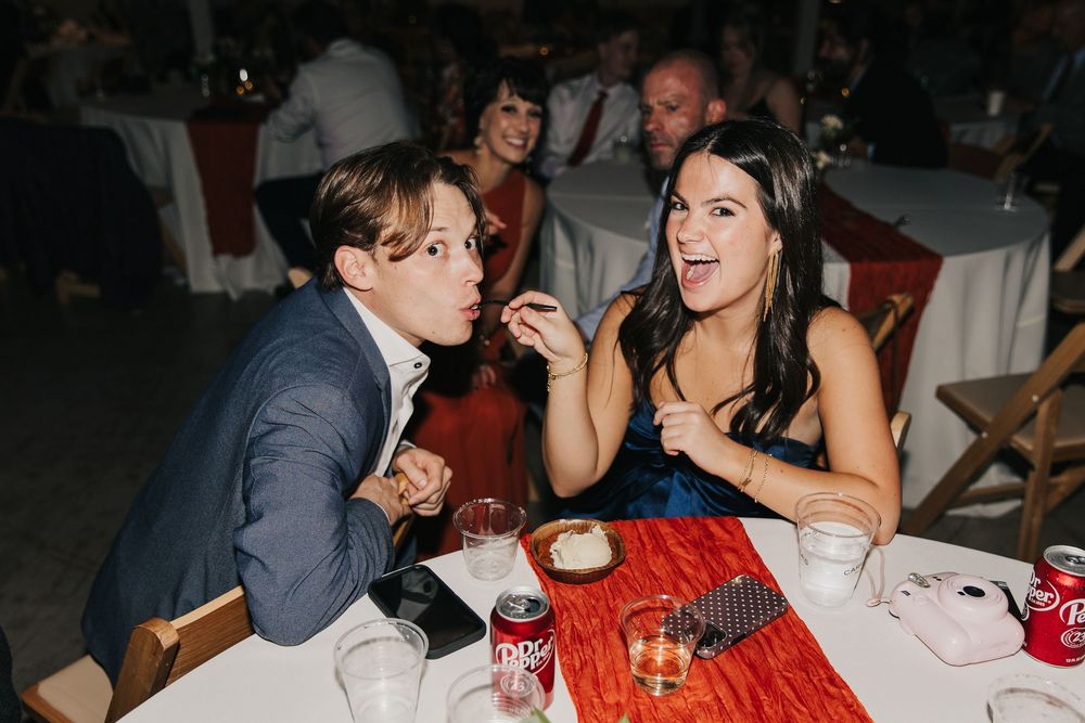 Two wedding guests share a laugh while sitting at a table with red decor and Coca-Cola cans.