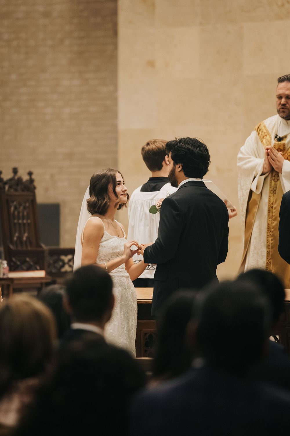 A wedding ceremony in progress at a church with a priest in golden robes and guests watching from the pews.