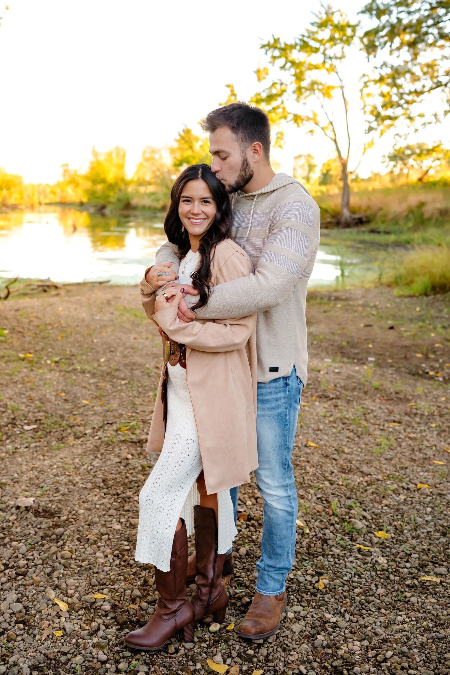 Romantic couple embracing outdoors during golden hour wearing casual autumn attire.
