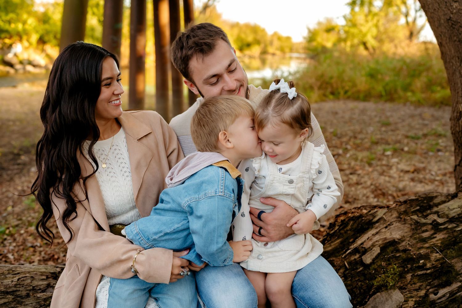 A family shares a tender moment together while sitting outdoors in golden sunlight among trees.