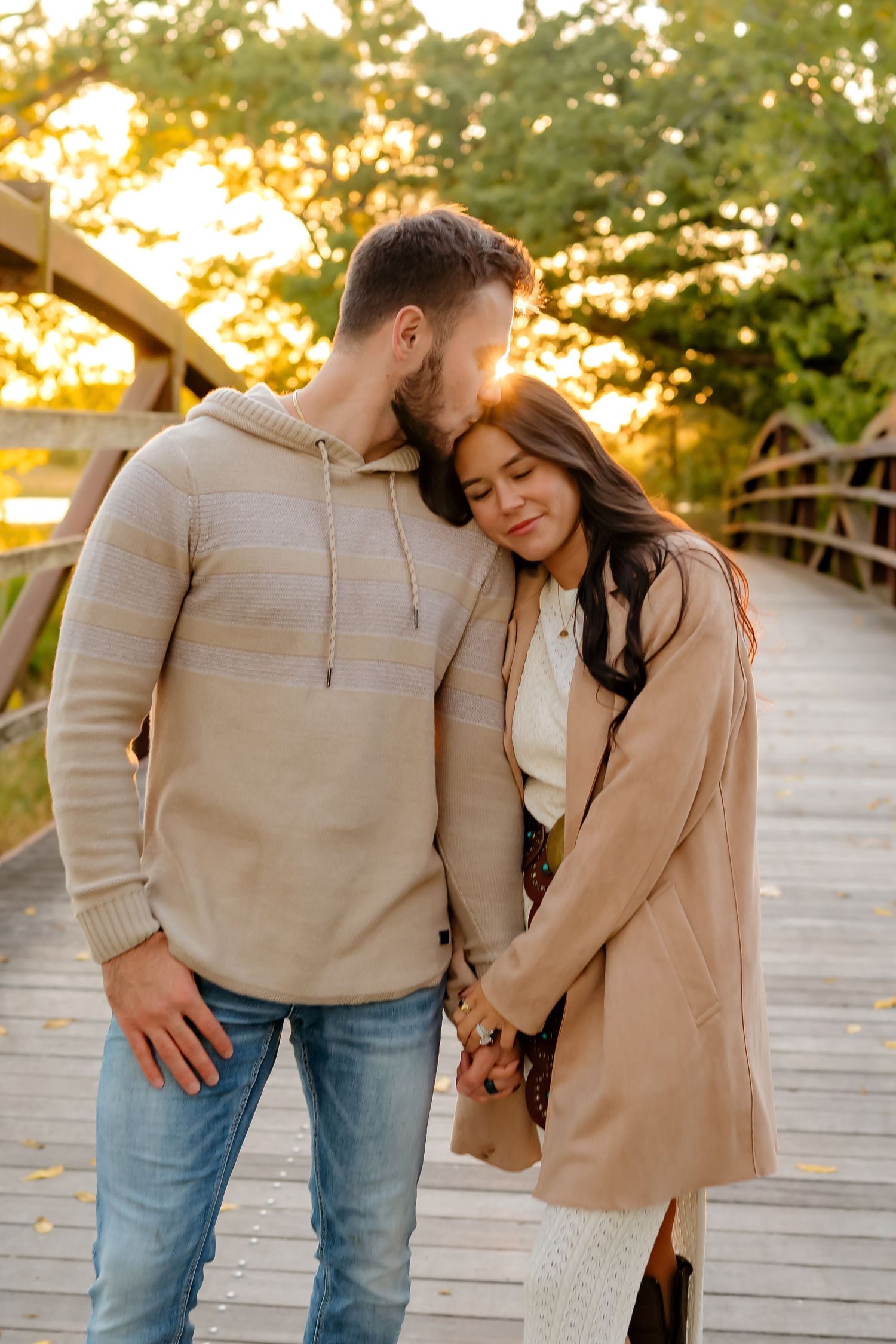 Couple sharing intimate moment on wooden boardwalk during sunset in casual fall clothing.