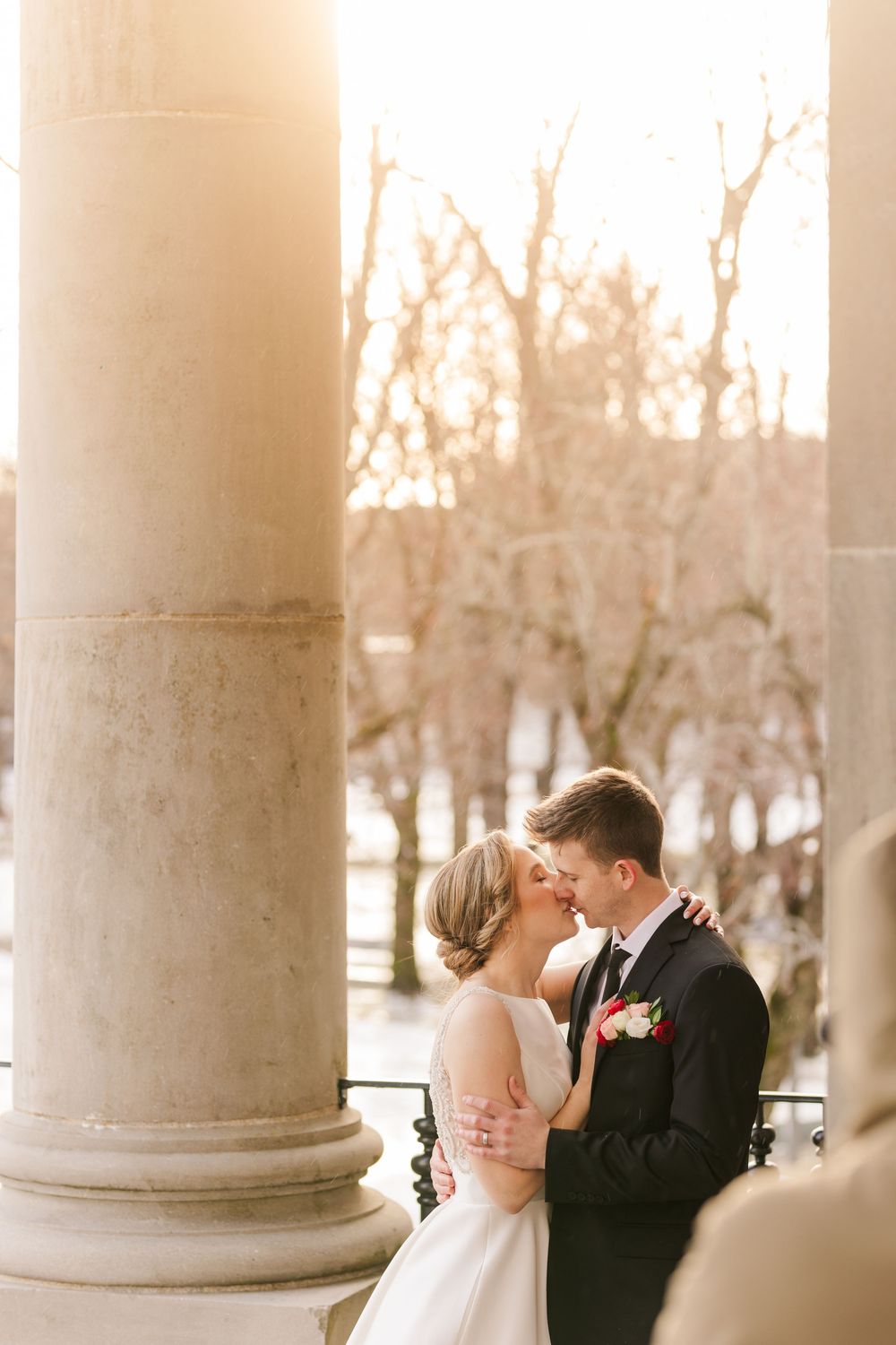 A romantic wedding couple shares tender moments between elegant white columns during sunset.