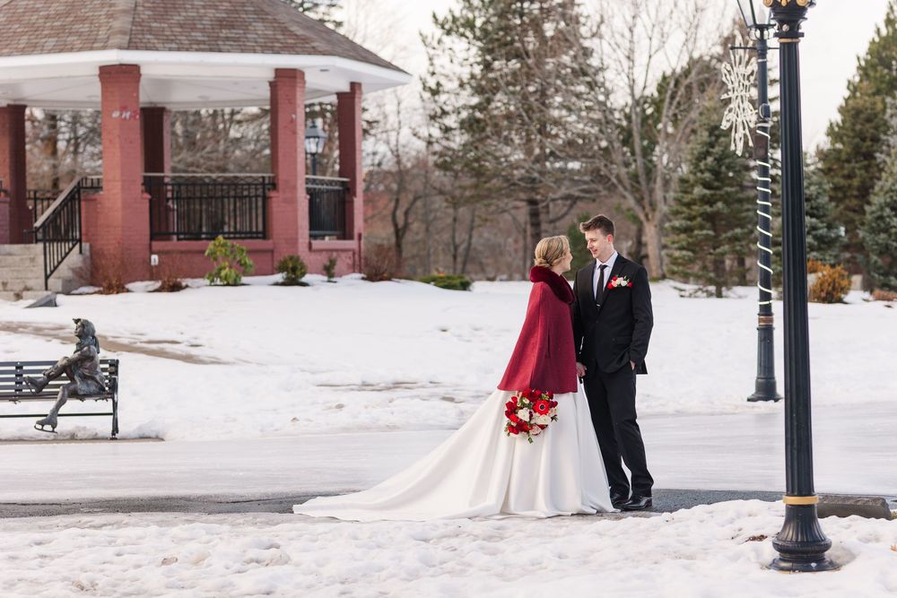 Winter wedding couple poses in snowy outdoor setting with brick buildings and lampposts in background.