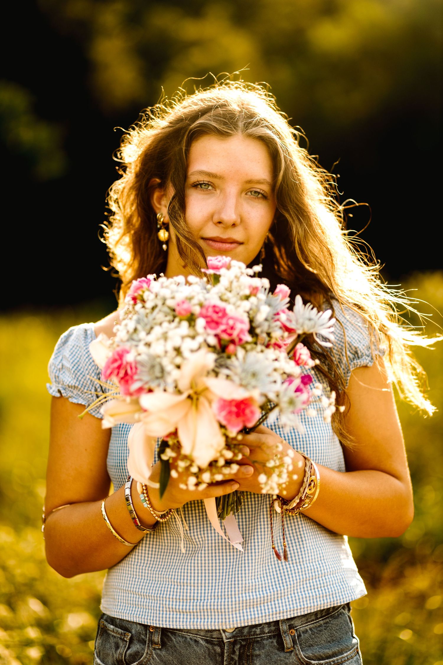 A person in a gingham top holds a colorful bouquet of flowers while backlit by golden sunlight in a garden setting.