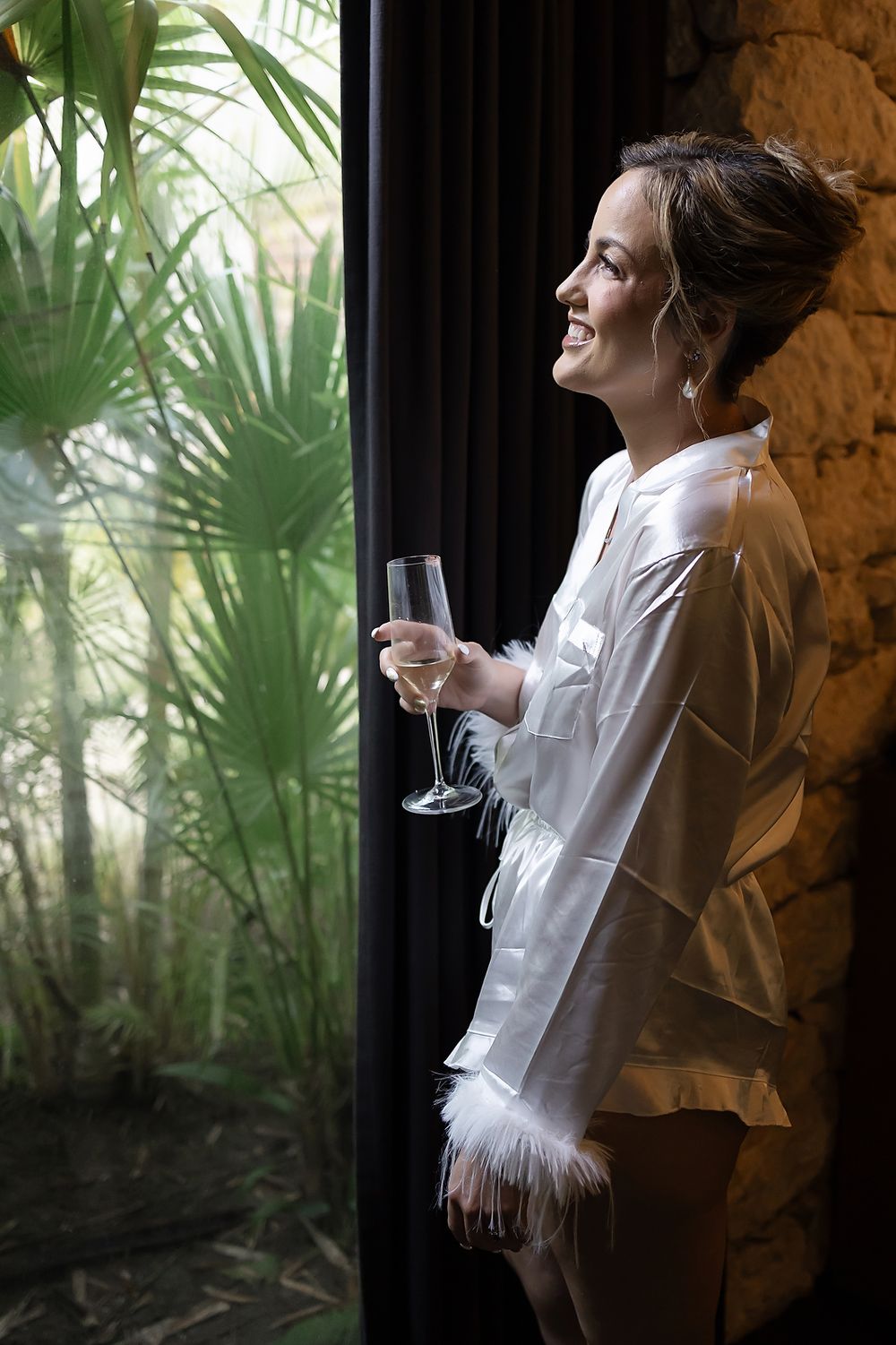 Bride standing by window with champagne during getting ready at Secrets Moxché.