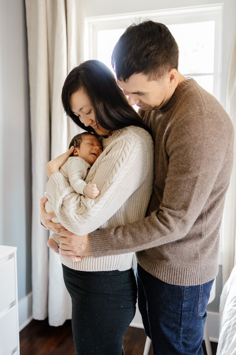 Parents hold their new baby in front of a window