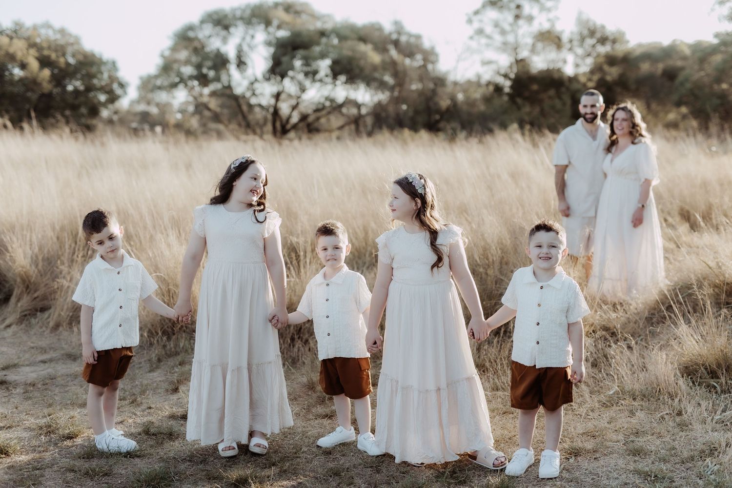 Family portrait sequence in natural field setting wearing coordinated white and neutral outfits.
