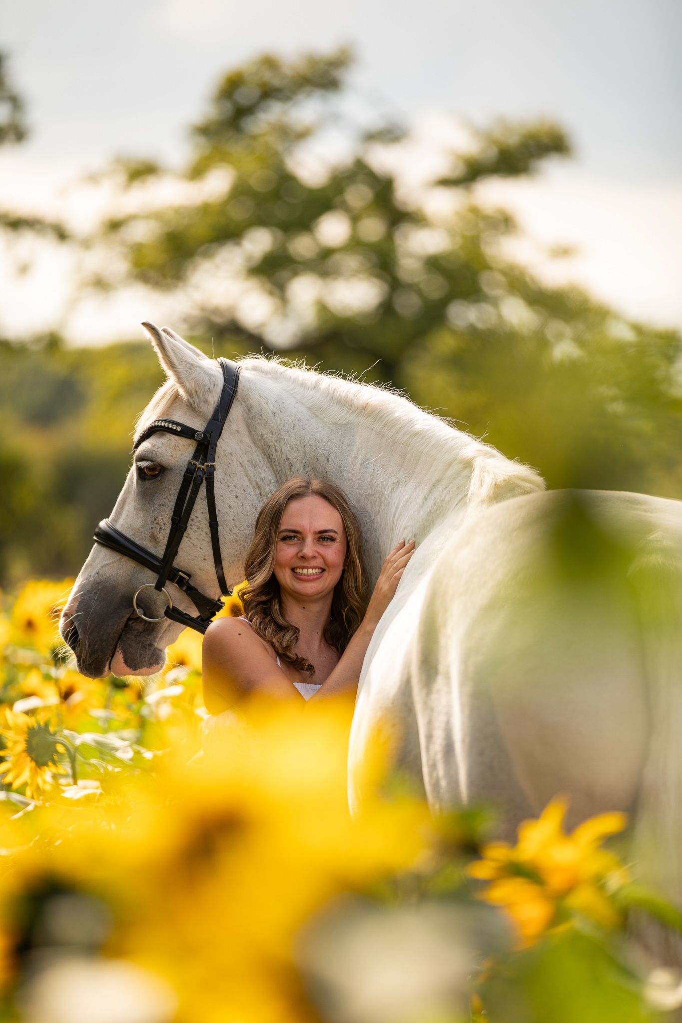 Young girl in denim overalls embraces a palomino horse in a sun-dappled forest setting.