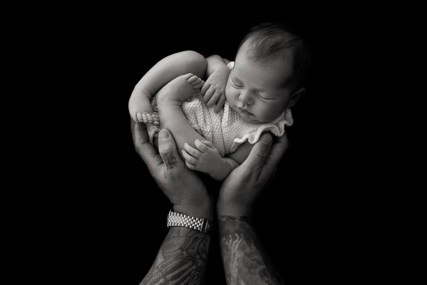 Black and white photo series showing tender moments while parents hold their newborn baby against dark background.