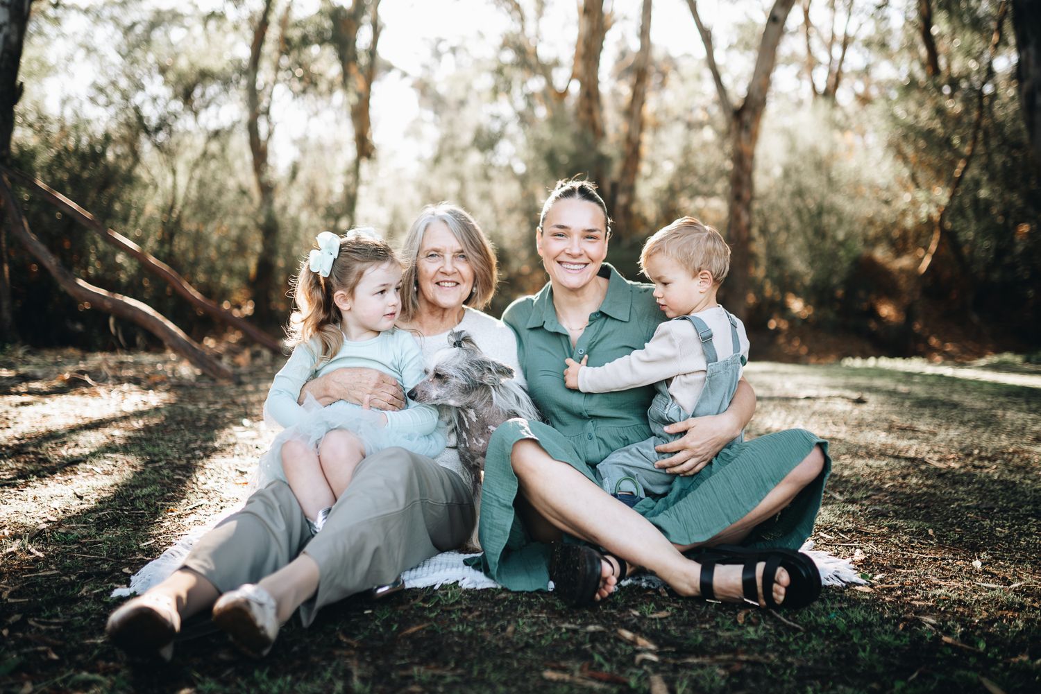 A 3 generation family group lounges together in a sunlit forest taken by a Melbourne family photographer.