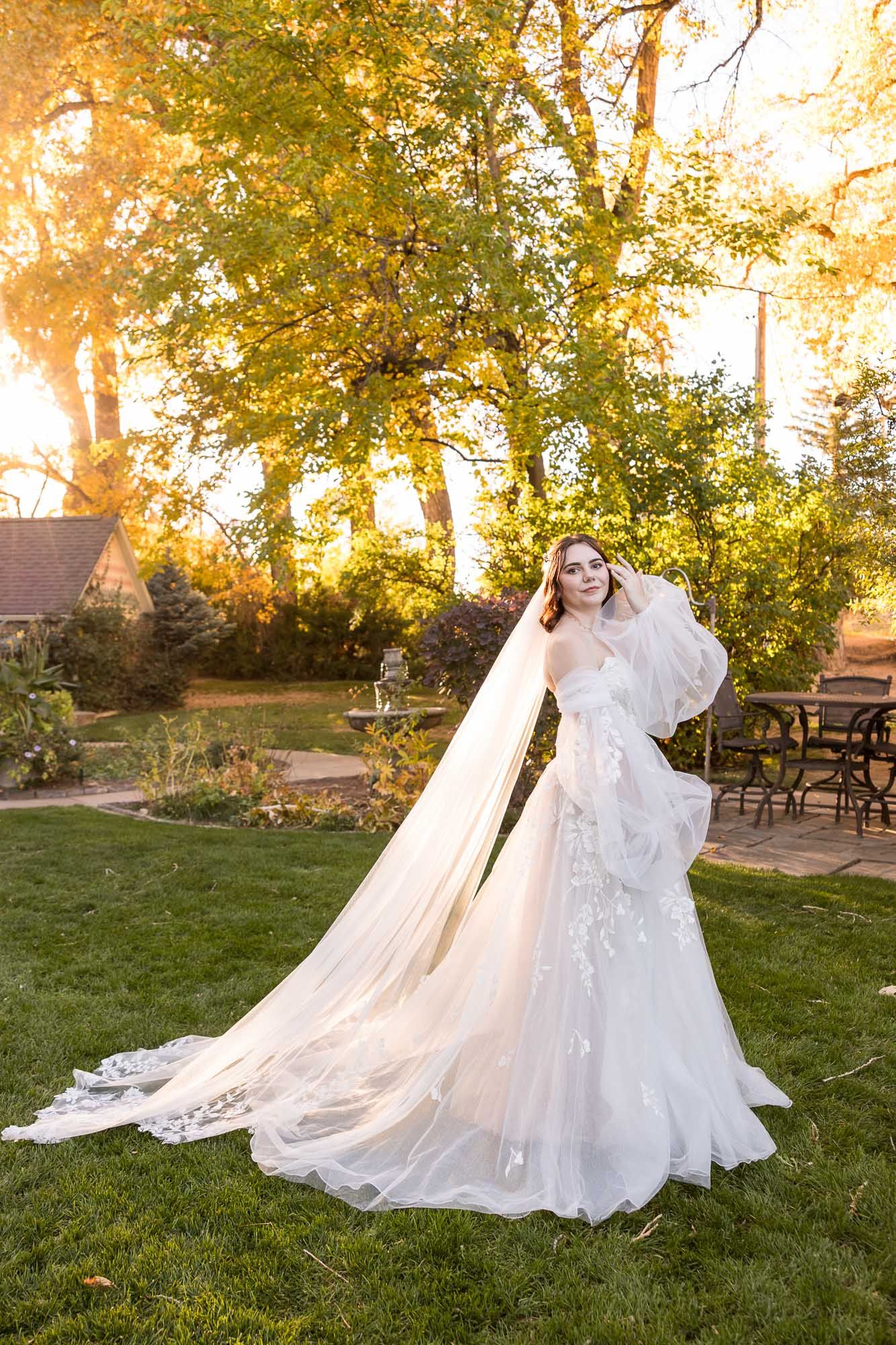 A flowing white wedding gown with a long train photographed in a garden setting at golden hour.